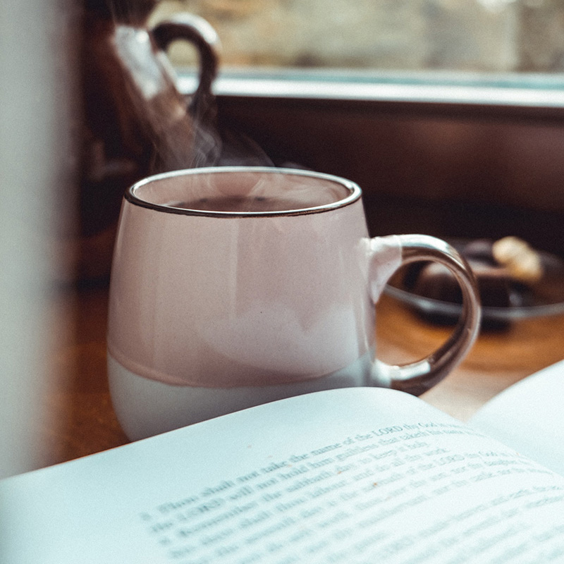 Open book sigging on a wooden table, next to a mug filled with a warm beverage.